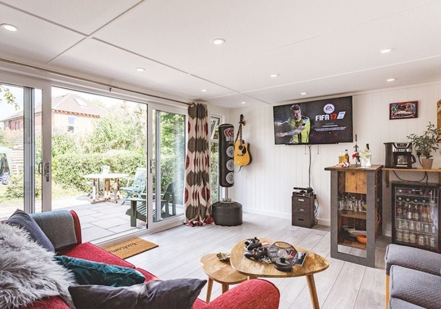 Spacious garden entertainment room featuring a home bar, gaming setup, red sofa and large sliding glass doors opening onto the patio.