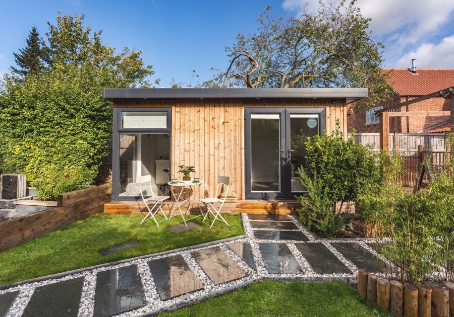 garden beauty room with timber cladding, glazed double doors and a landscaped garden featuring stone pathways and outdoor seating.