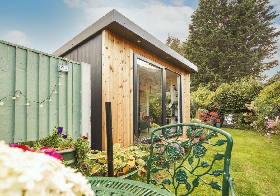 Contemporary Redwood-clad garden room with anthracite grey sliding doors, surrounded by flowers, greenery and outdoor seating.