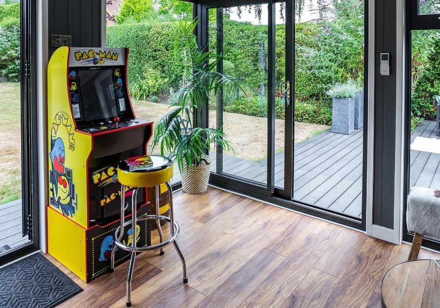 Modern garden games room featuring a retro Pac-Man arcade machine, wooden flooring and large glass doors overlooking the garden.