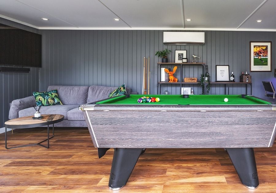 Spacious garden games room featuring a green-felt pool table, grey sofa, dark grey panelled walls and contemporary furnishings.
