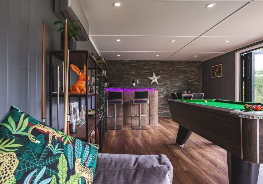 Bespoke garden entertainment room with a pool table, rustic home bar, exposed brick feature wall and purple LED lighting.