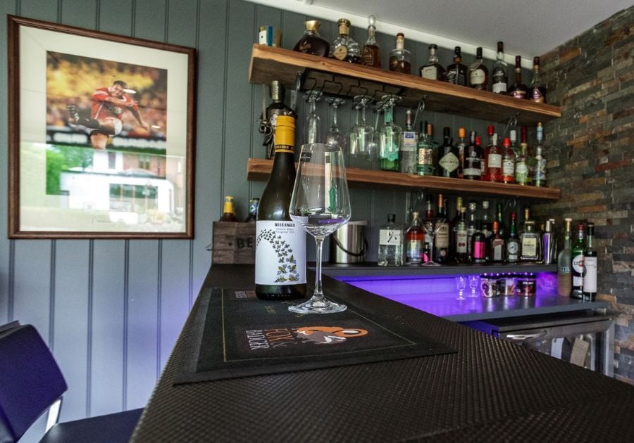 Bespoke garden bar featuring rustic wooden drinks shelves, a black bar counter, exposed brick feature wall and purple LED lighting.
