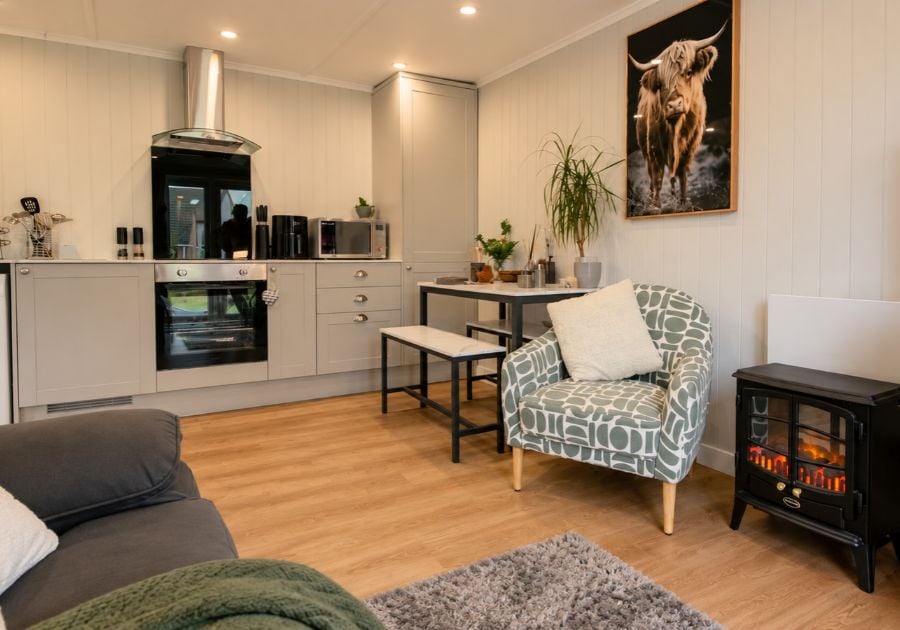 Modern garden annexe interior featuring a fully fitted kitchen, compact dining area, comfortable armchair and electric fireplace.