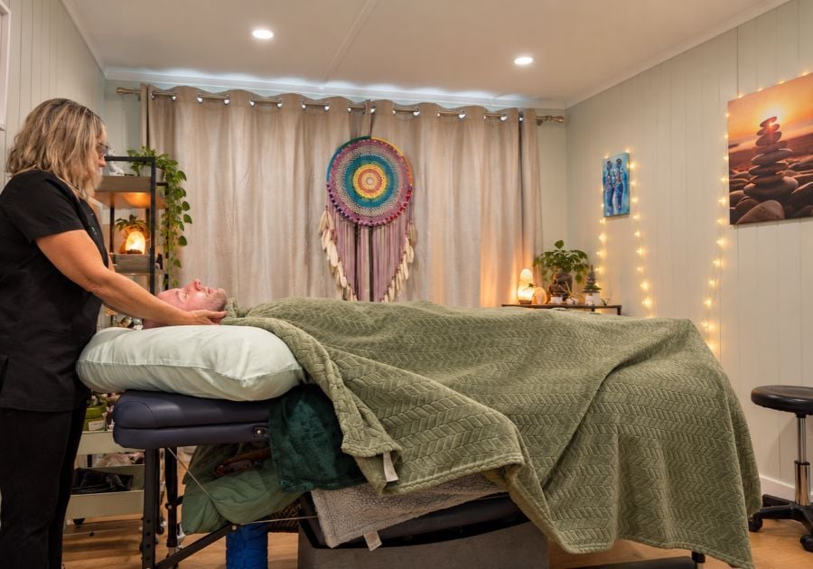 Relaxing garden therapy room featuring a therapist providing a holistic treatment to a client on a massage bed, with soft lighting and calming décor.