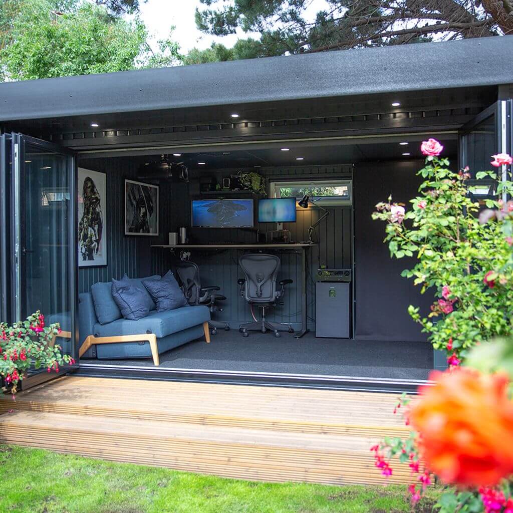 a patio area with a black marley garden room with open bi-fold doors in it with a blue couch and desk