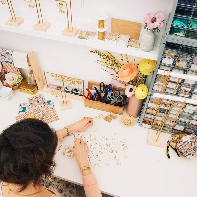 Interior of a hobby room for sewing with woman at desk with fabrics & threads