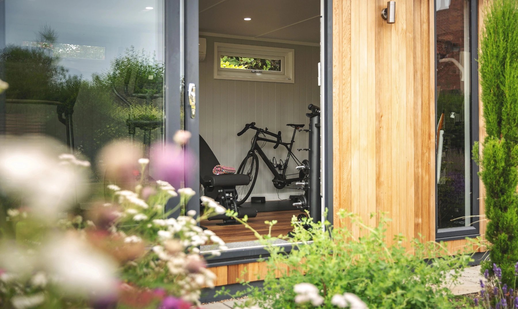 Luxury garden room gym in cedar cladding with garden flowers next to it