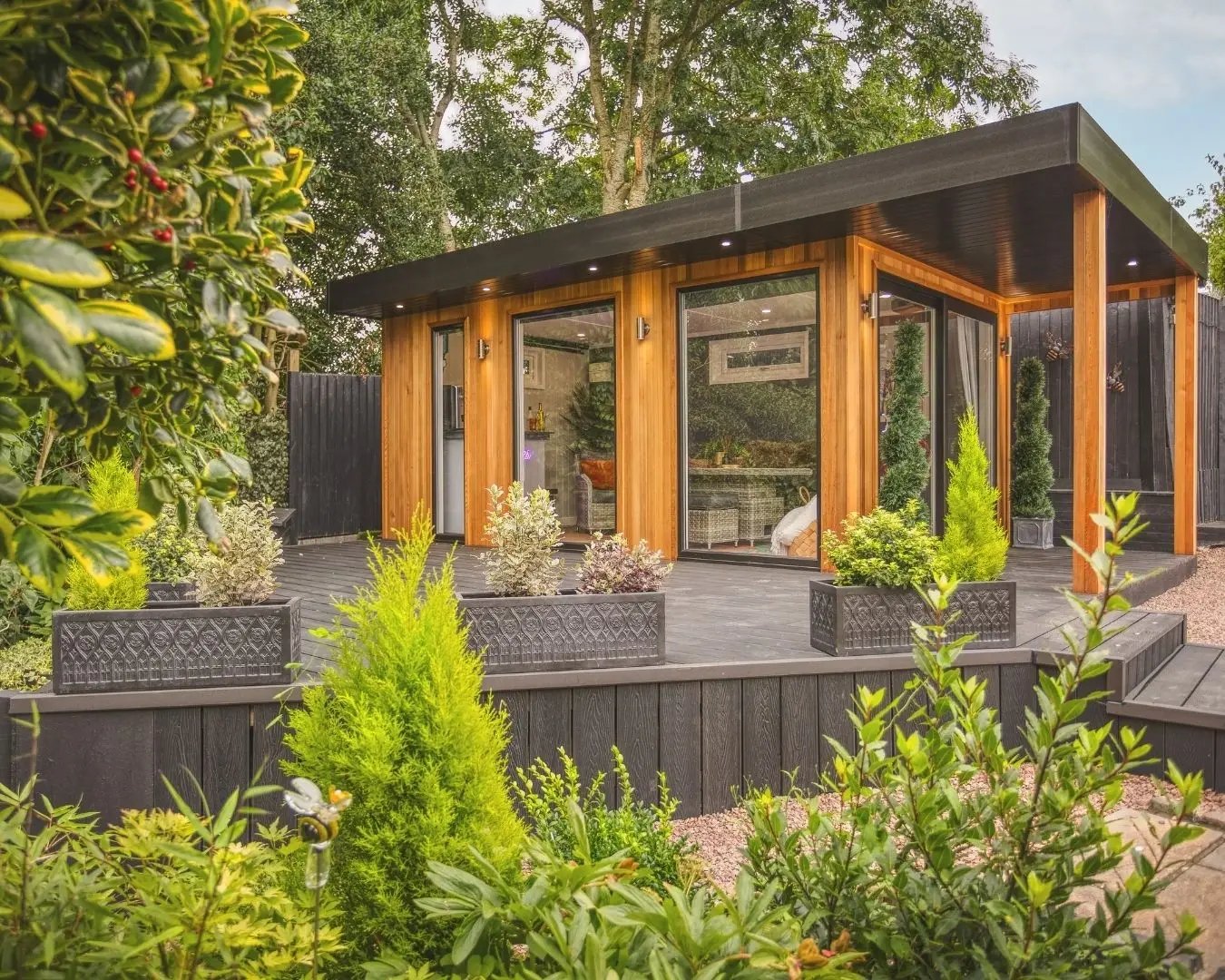 Contemporary wooden garden room surrounded by greenery, featuring floor-to-ceiling windows and outdoor decking