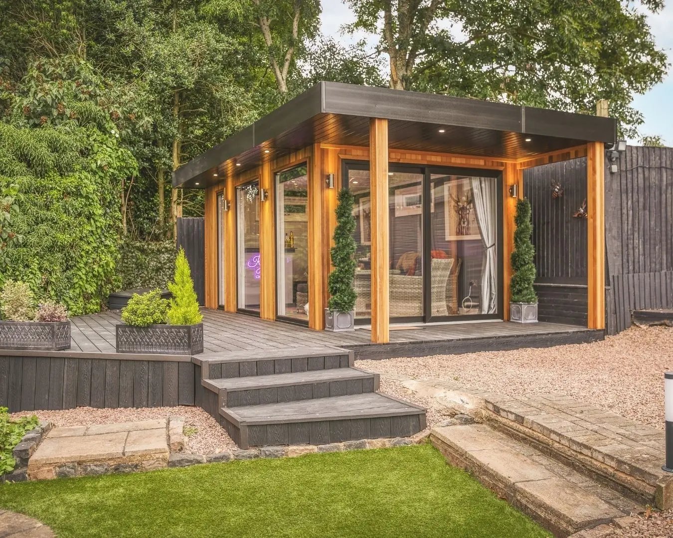 Modern garden room with timber cladding, large glass doors, and raised decking in a landscaped garden