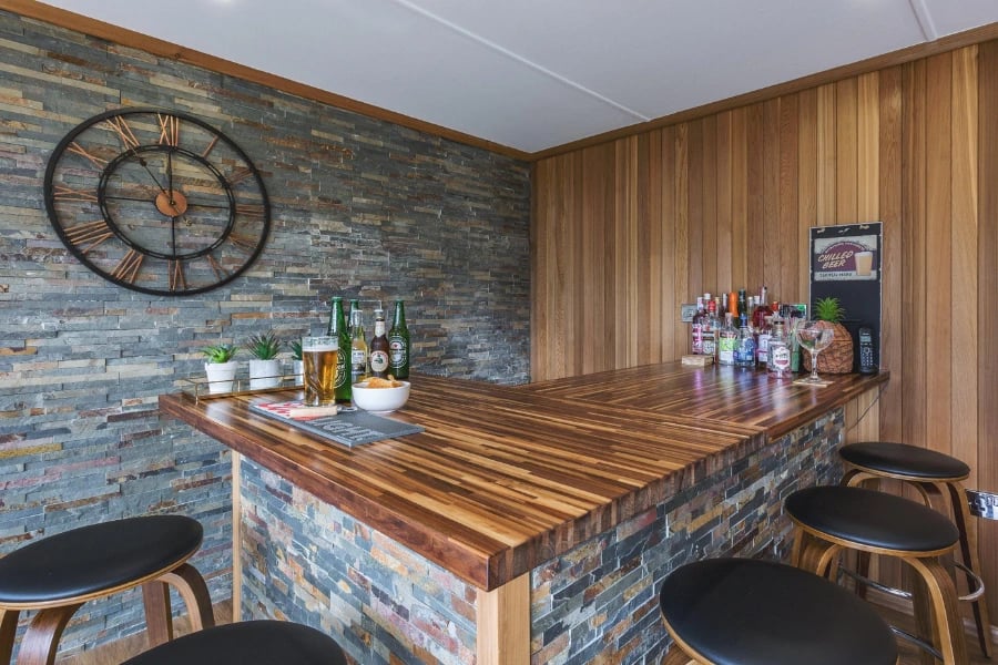 large garden bar with slate feature wall and wooden table top with various bottles of beer and spirits on top of it