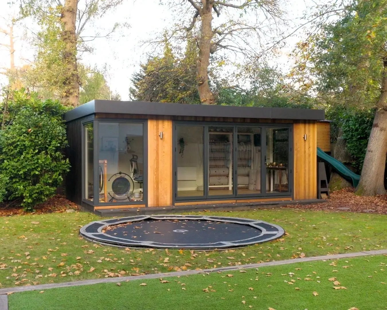Modern garden room with floor-to-ceiling glass doors, timber cladding, and a flat roof, set in a landscaped UK garden