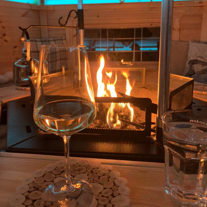Interior shot of a bbq cabin lit with glass of wine on the tray table next to fire
