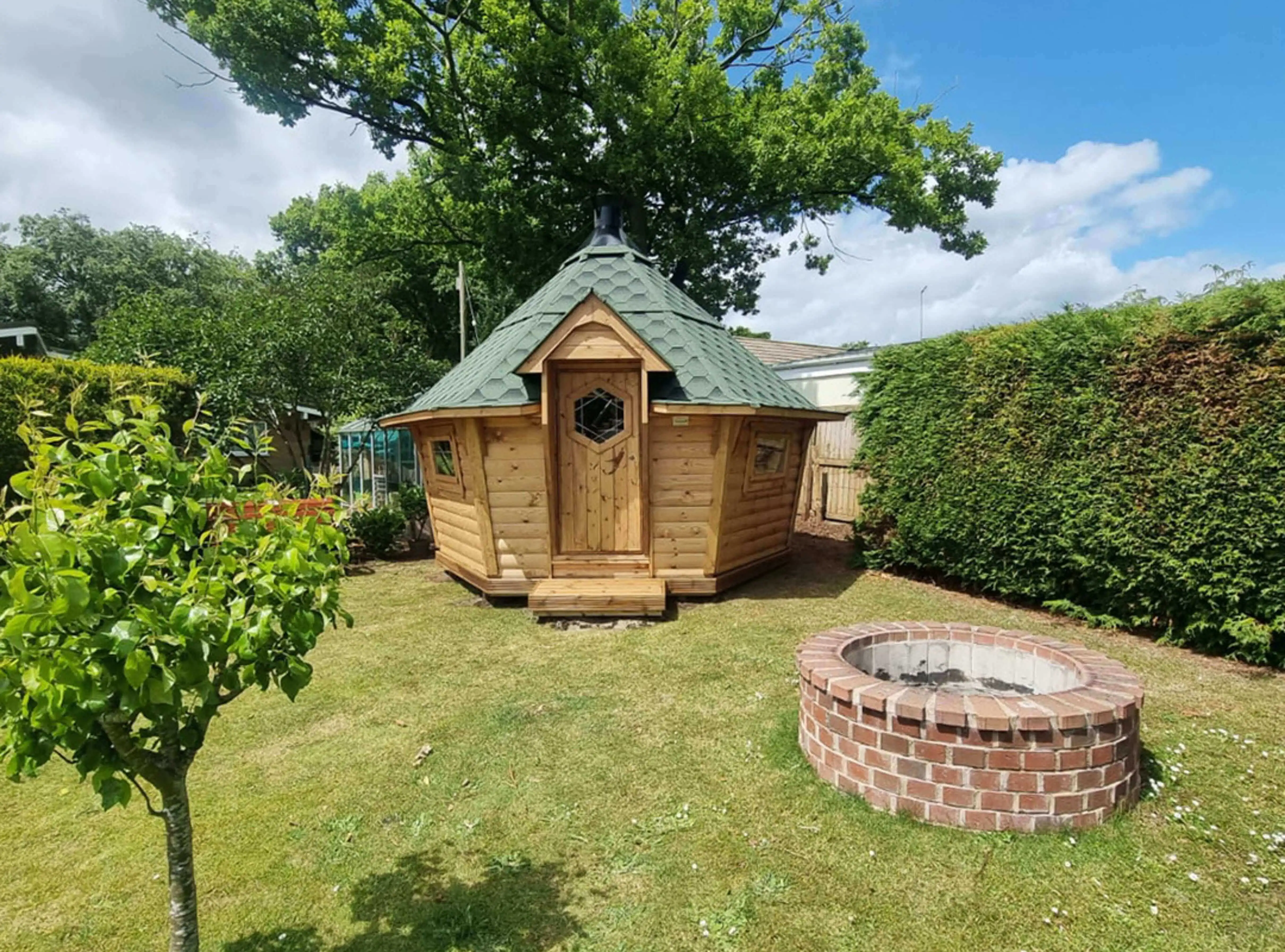 Arctic Cabin with green roof in garden with blue sky and trees and grassy area and concrete well and tree