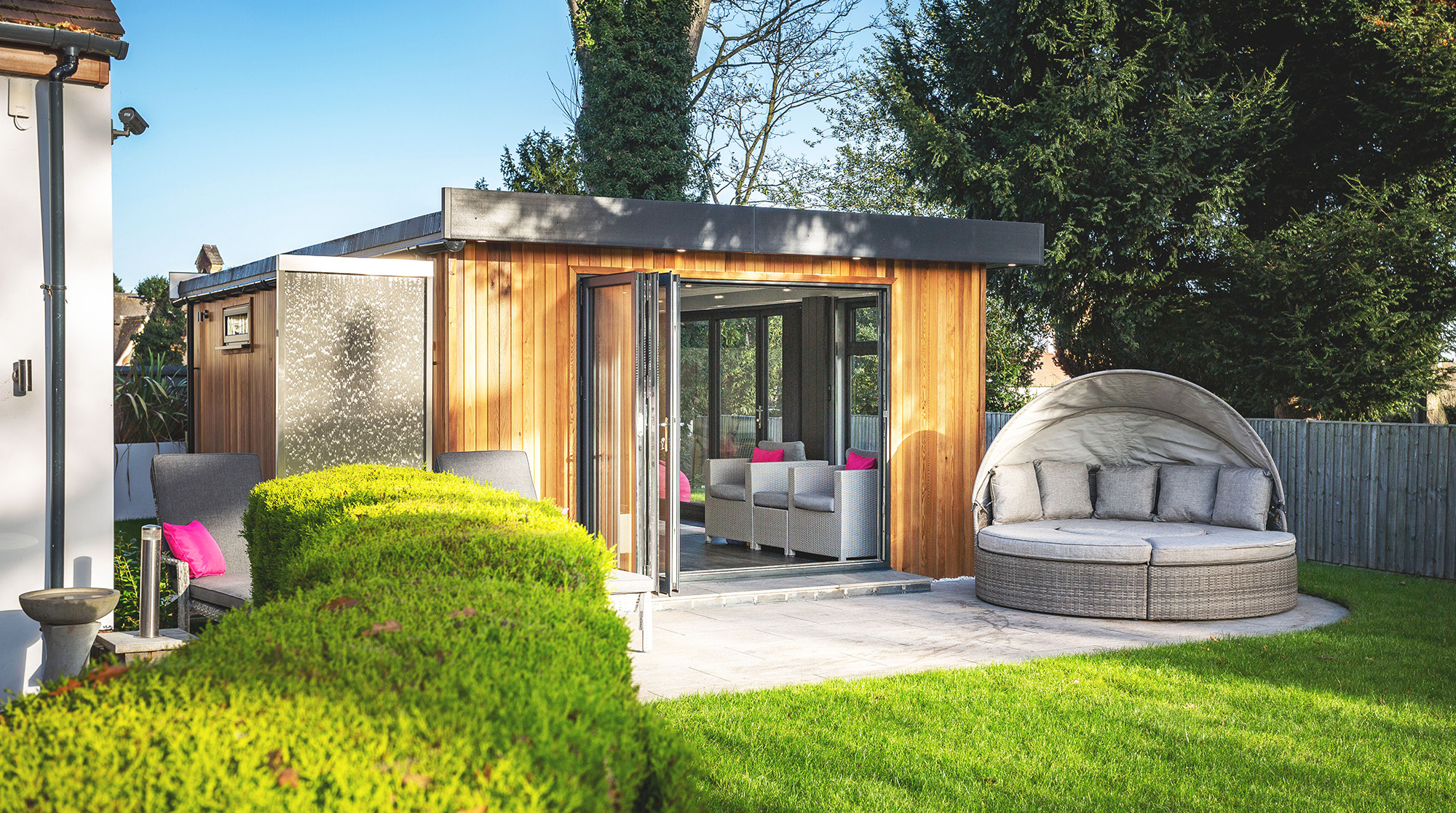 Exterior of a cedar garden room with bi-fold doors open and garden furniture outside