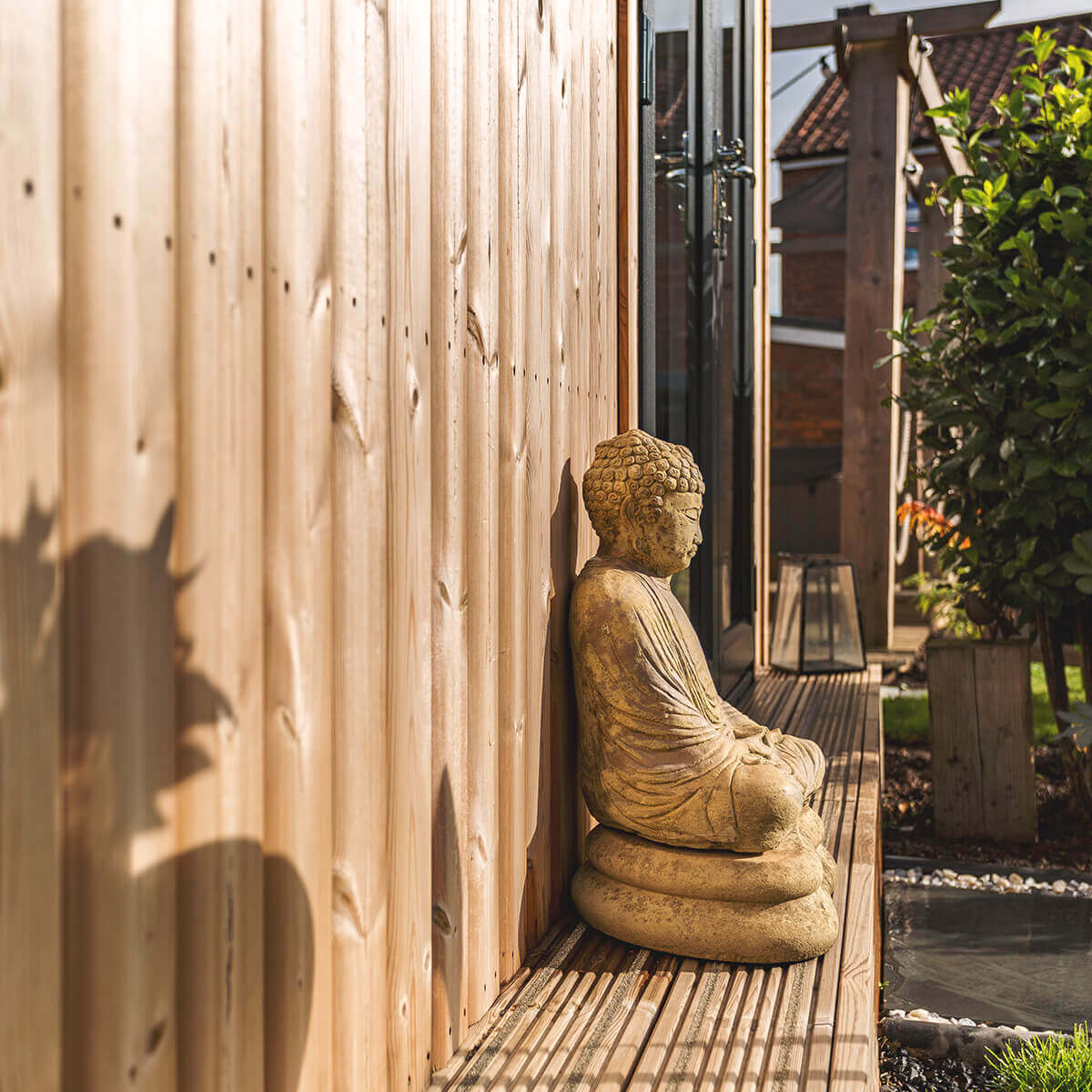small wooden buddha statue outside redwood garden room with lawn area 