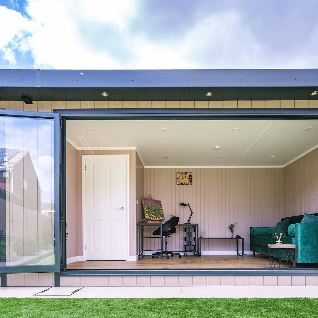 external view of garden room with open bi-fold doors and partition doors and large green velvet sofa and office furnishings