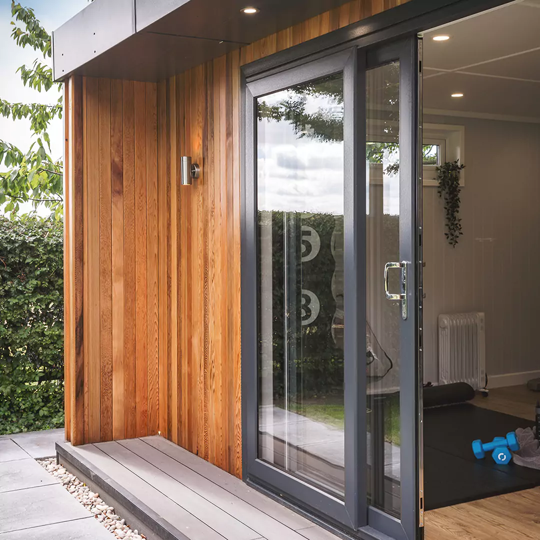 Cabin Master Cedar Multi Use Gym and Office external shot with sliding doors open and patio and garden hedge in background