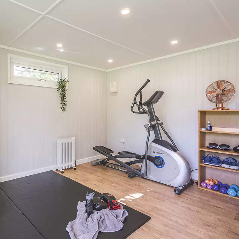 Cabin Master Internal View of Garden Gym with elliptical machine and mat space and indoor plant with furnishings and window