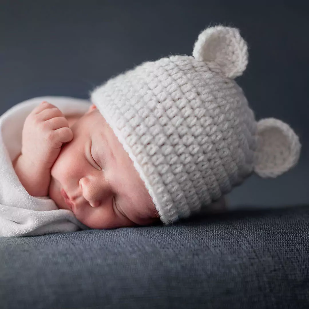 Newborn baby asleep as part of photoshoot, with hat & blanket