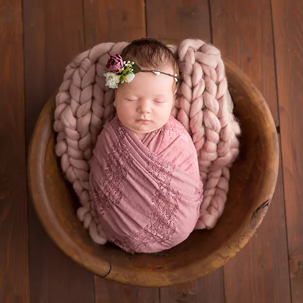 Image of a newborn baby girl at photoshoot swaddled in pink muslin blanket