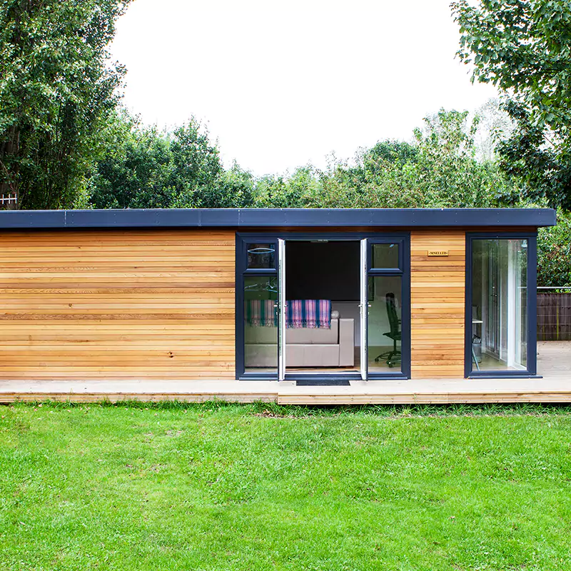a large garden cinema room timber building on top of timber decking with large green lawn area and sliding glass doors