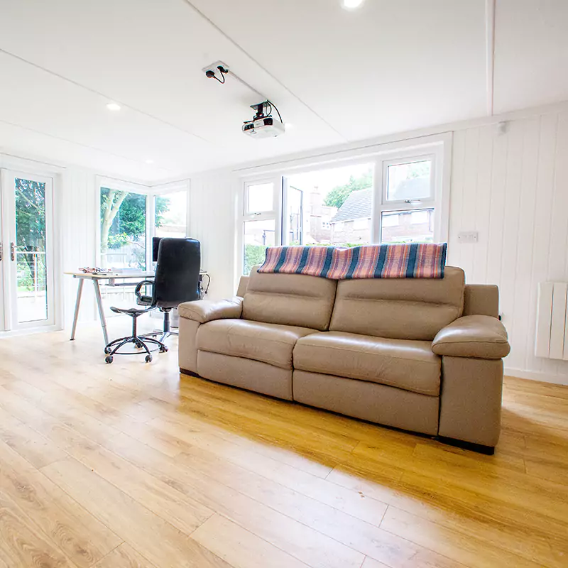 a white couch with a plaid blanket on top of it inside a garden cinema room with large projector screen