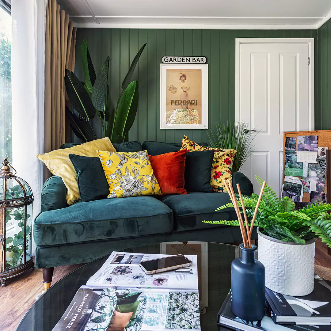 Interior of a garden room with dark green feature wall, tropical plant and plush velvet sofa
