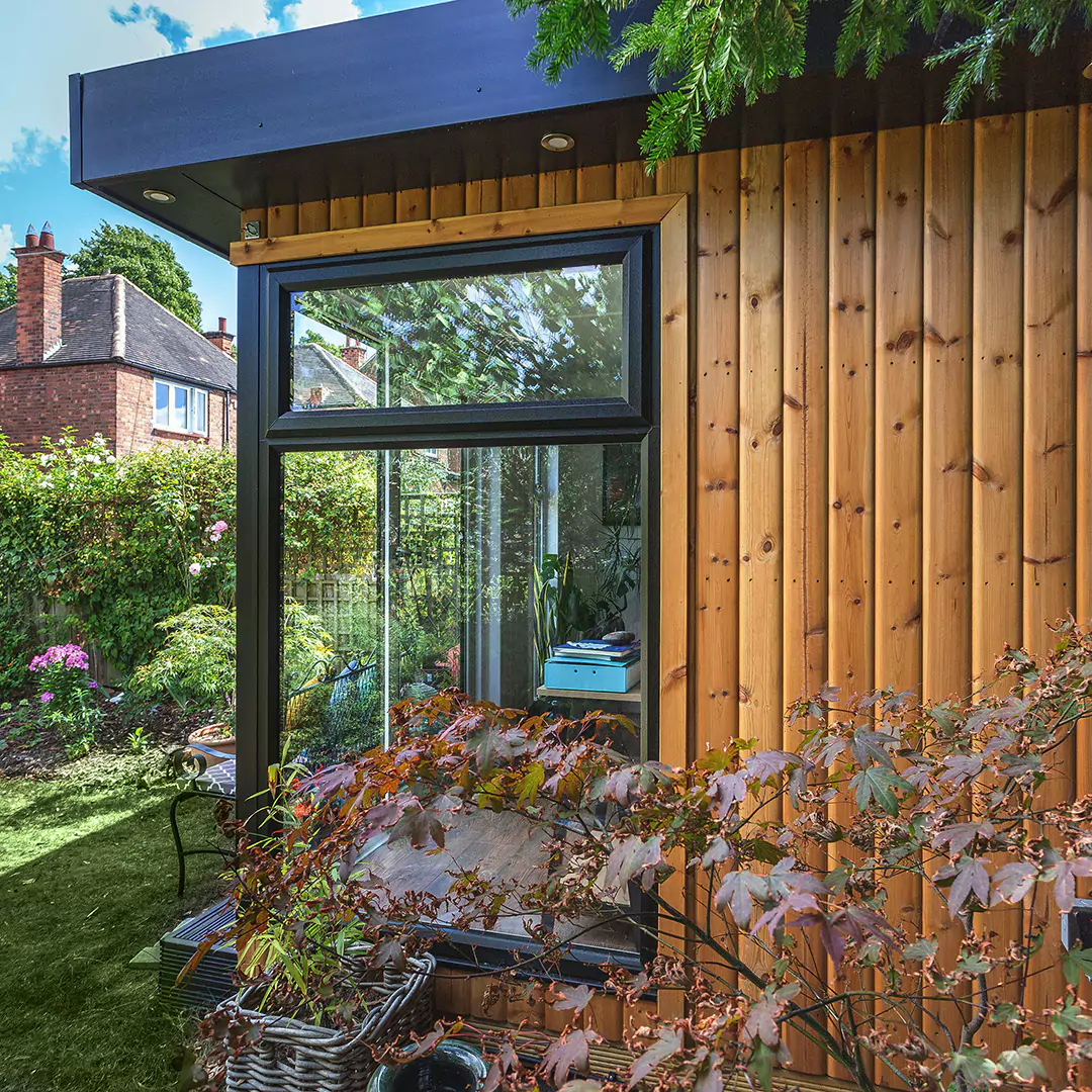 Garden Office with green lawn and bench area with brightly coloured cushions and flower bed