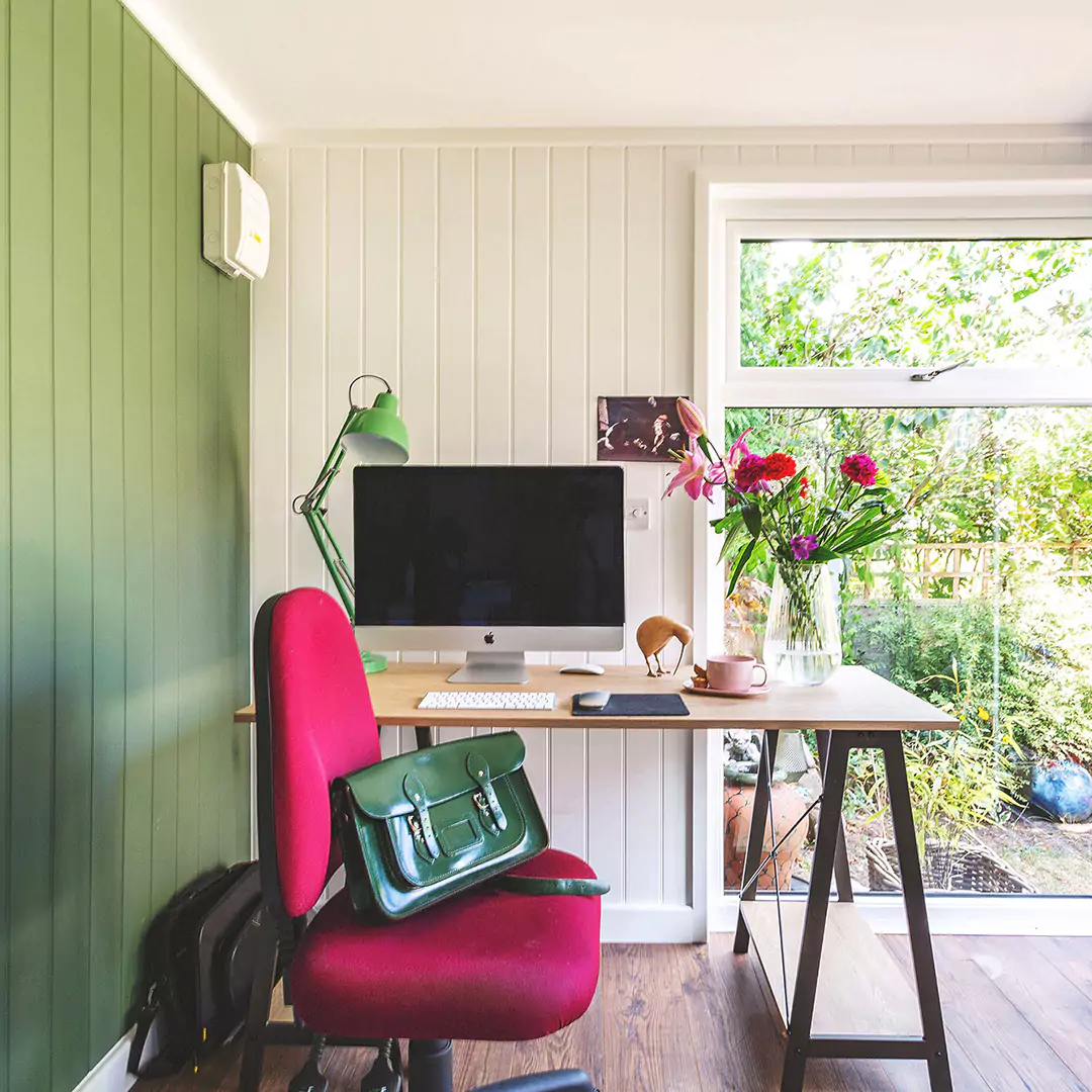 inside view of garden office with bright pink desk chair and desk with mac computer and vase of roses