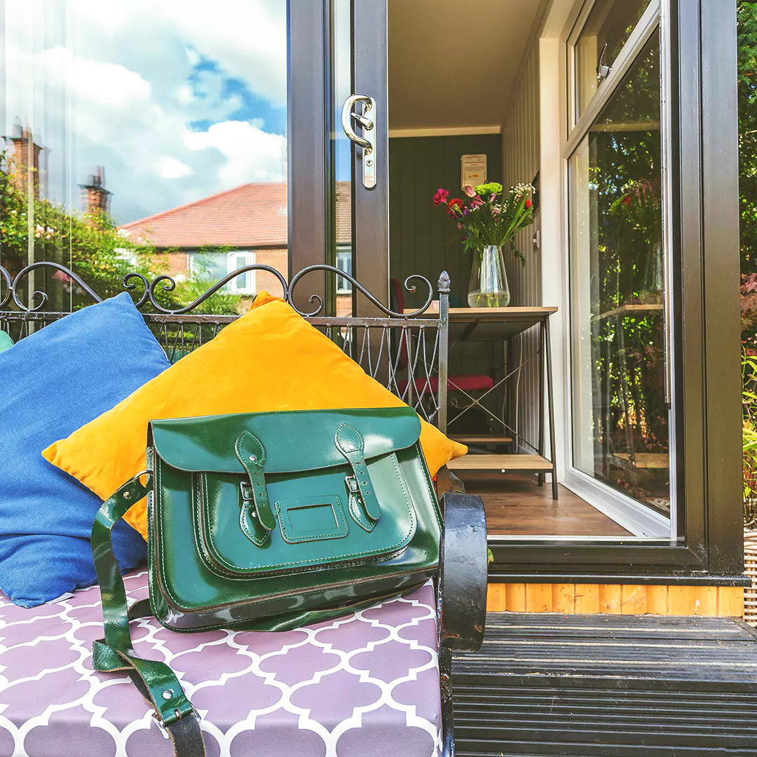 small garden office with bench and blue and yellow cushions on it with green patent satchel and table with vase of flowers on it 