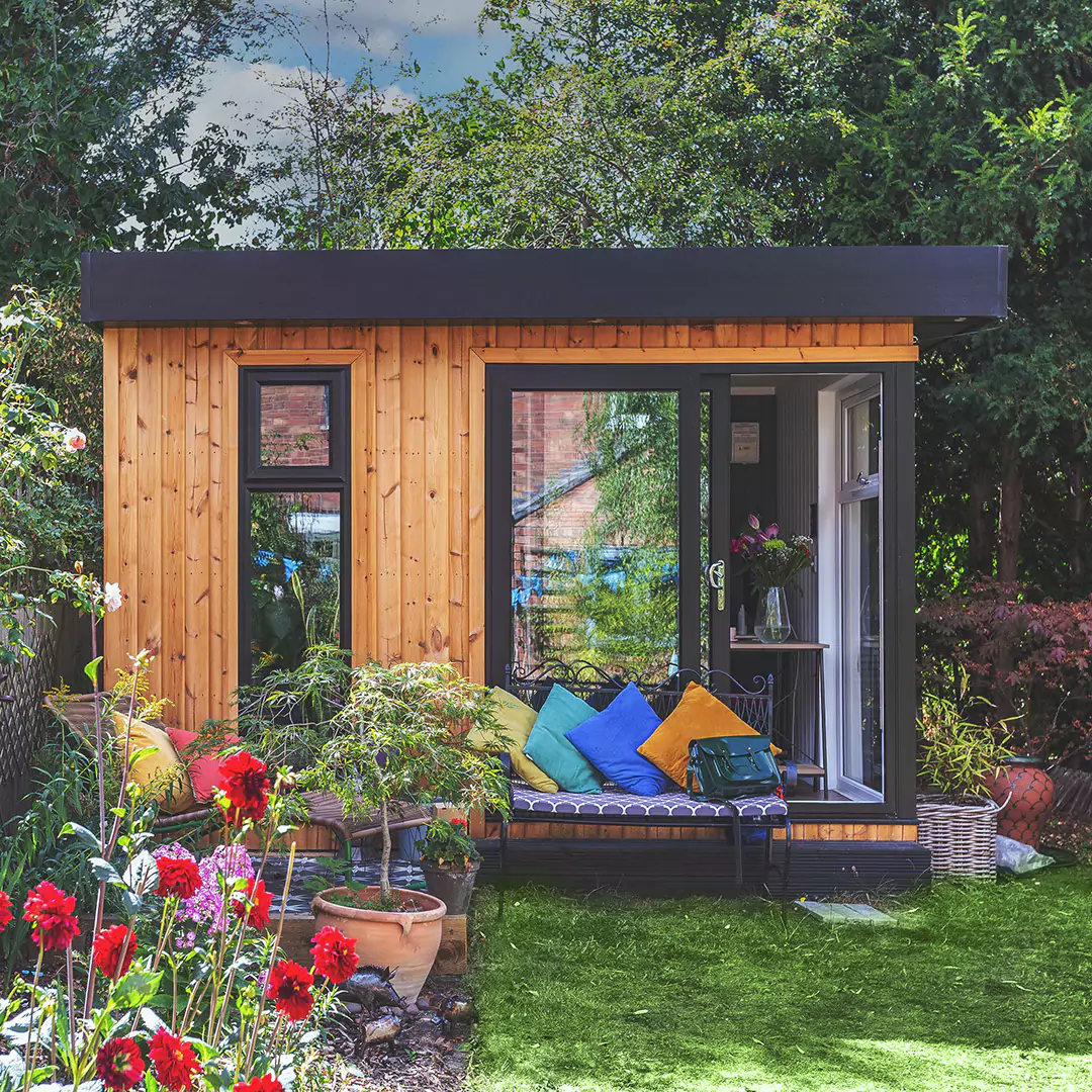 Garden Office with green lawn and bench area with brightly coloured cushions and flower bed