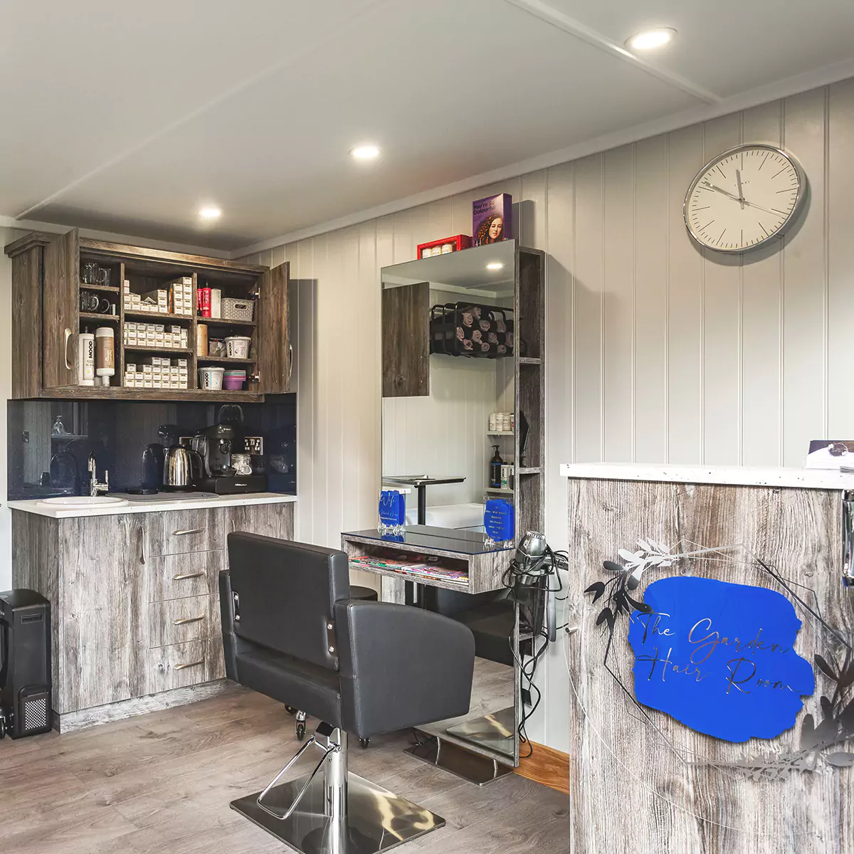 Hairdresser Salon with marble worktops and shelving and large vanity mirror with black leather hairdresser chair and wall clock