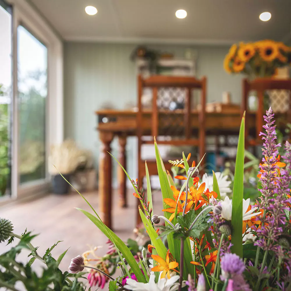 garden room with sunflowers in a vase on top of table with view of lawn and hedges