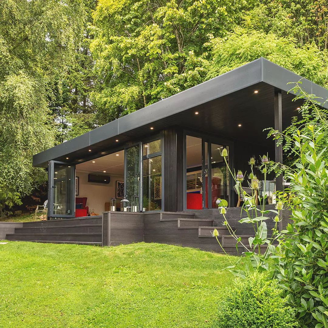 a black marley garden room with veranda in lawn area with a red chair in the window