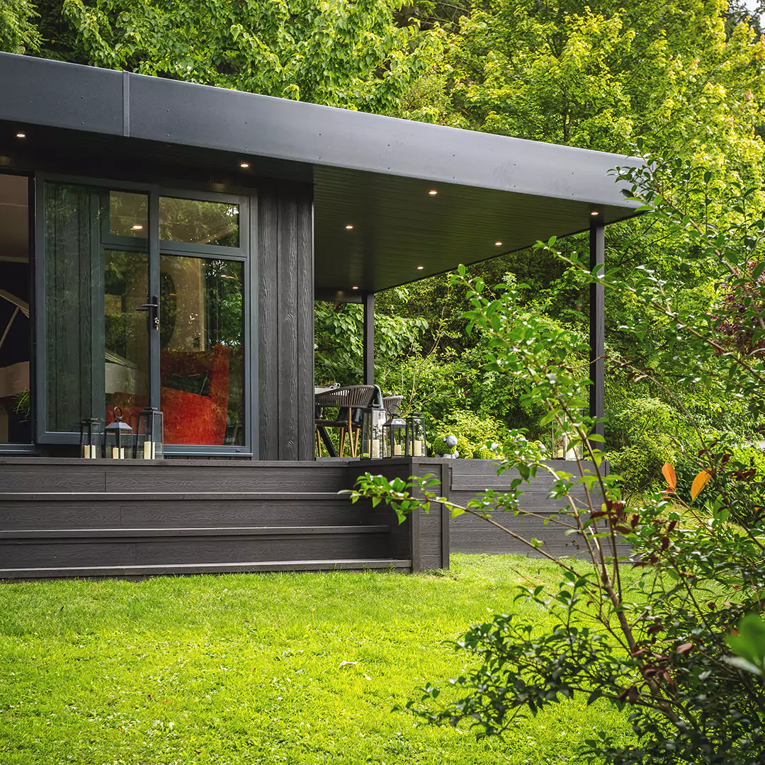 a black marley garden room with veranda in lawn area with a red chair in the window