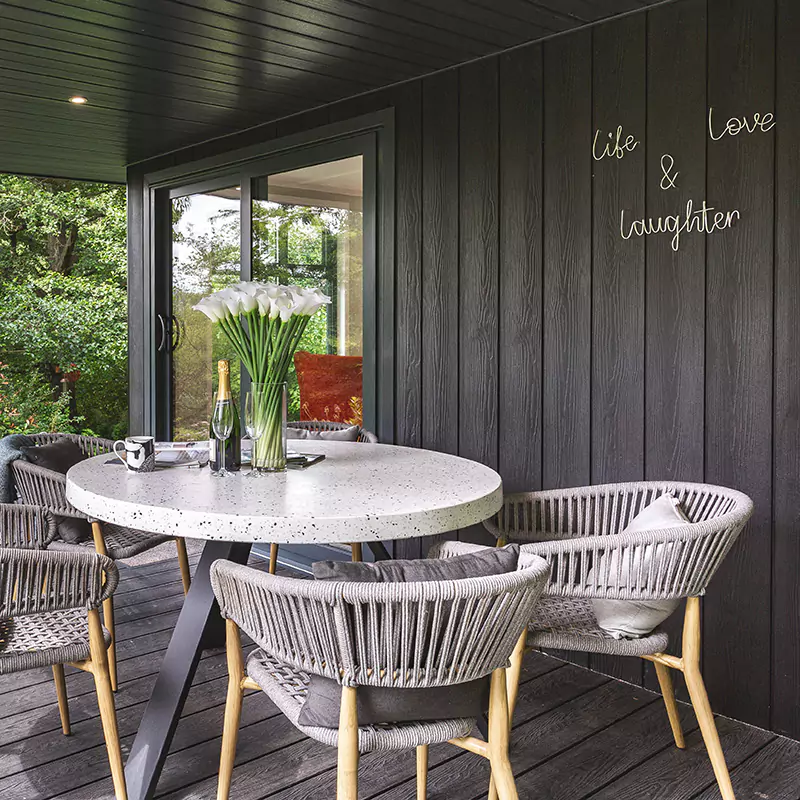 a table with four chairs and a vase with flowers on it on a veranda