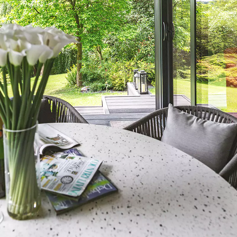 a table with two chairs and a vase with flowers on it on a veranda