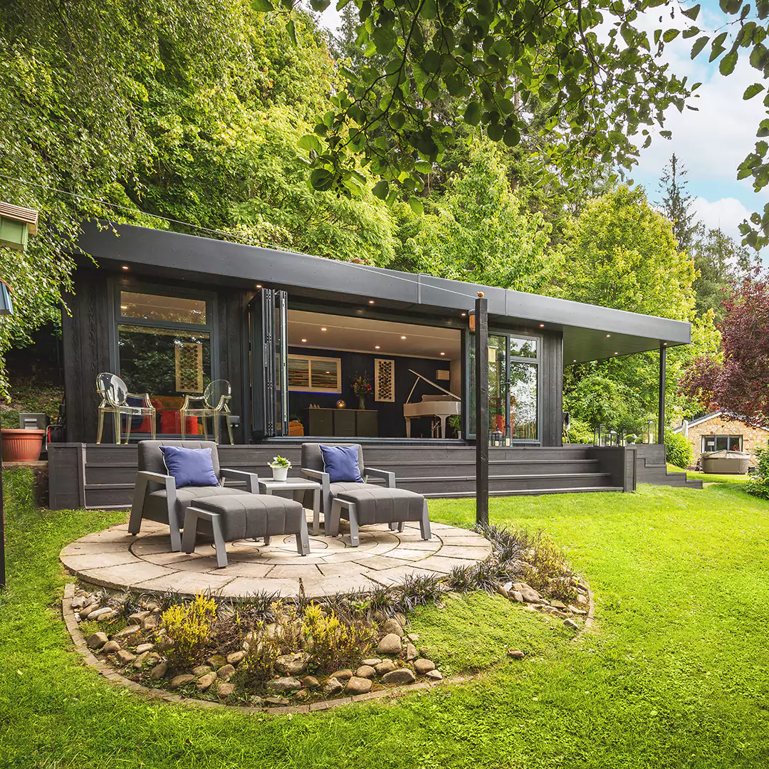 Black Marley Garden Room With Veranda and large lawn area with rattan garden furniture and patio area with weeds and rocks