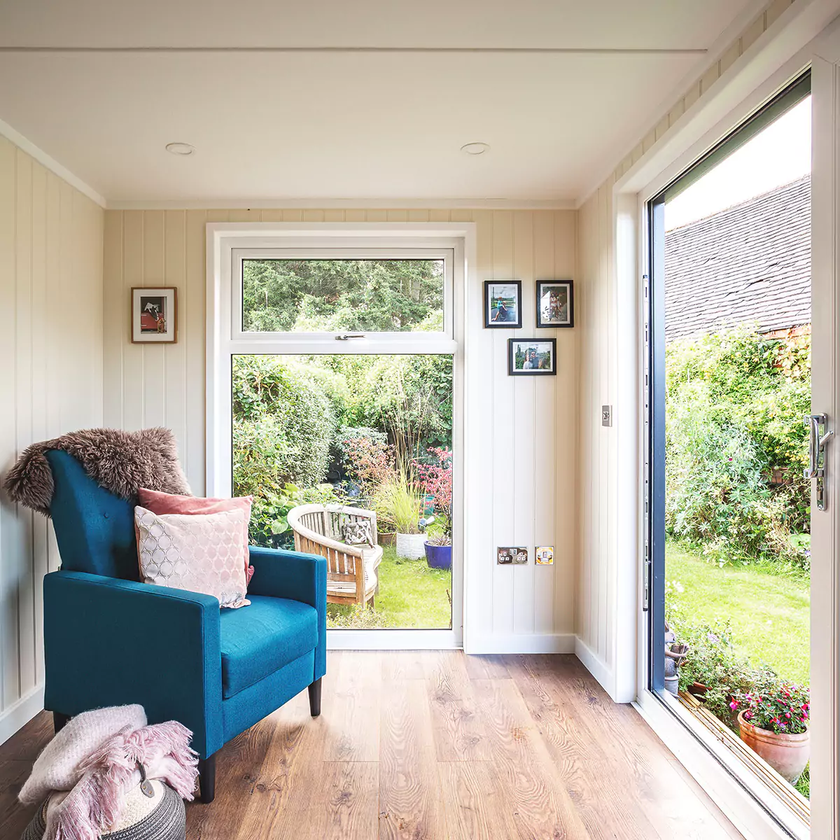 small garden summerhouse with view of lawn area with blue velvet armchair and picture frames on wall 