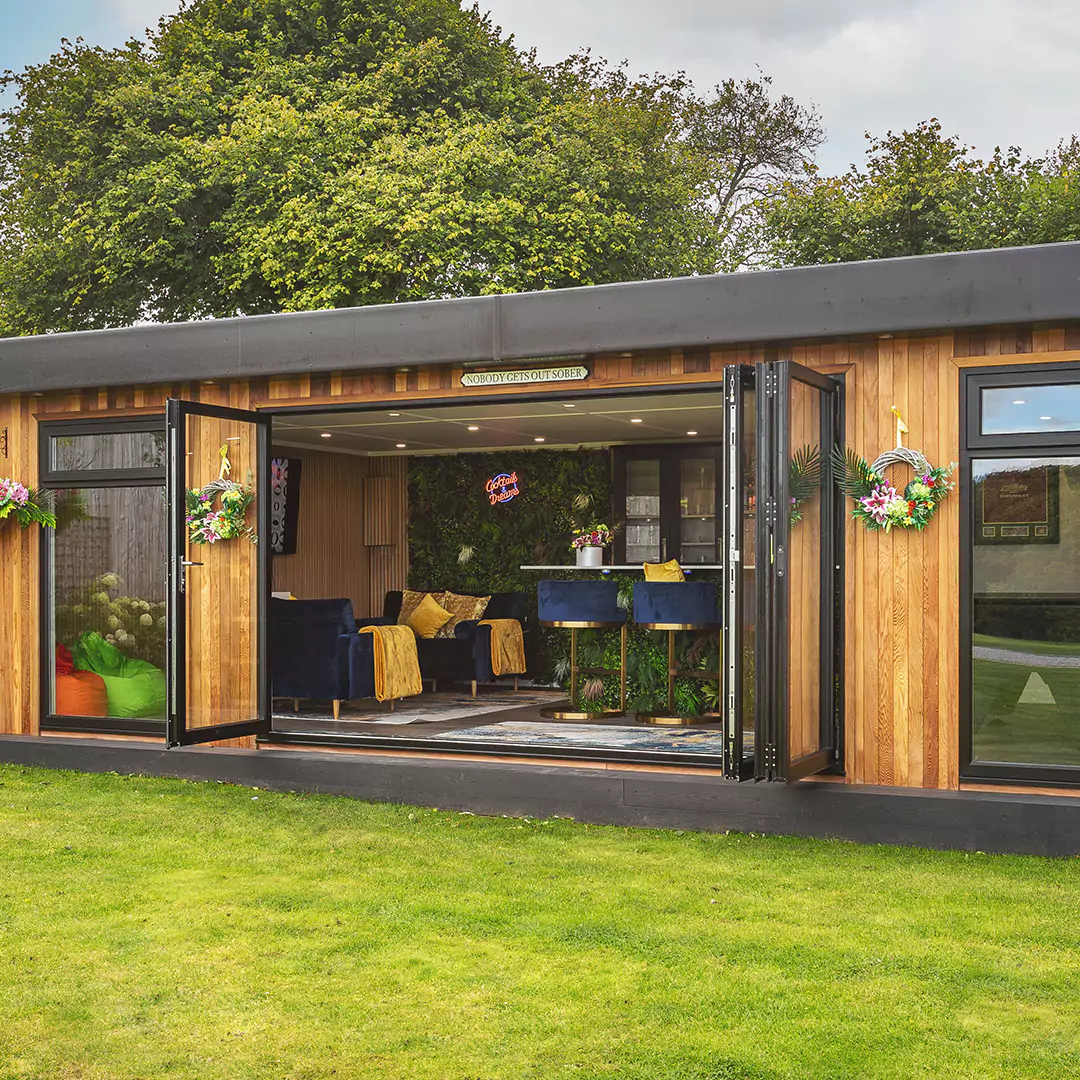 a cabin master garden bar with large glass windows and hanging baskets