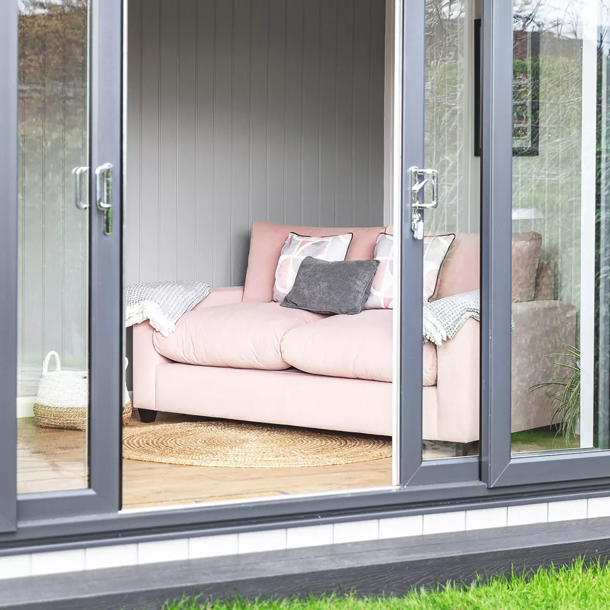 sliding glass doors with view into garden room office space with small pink couch and grey sofas 