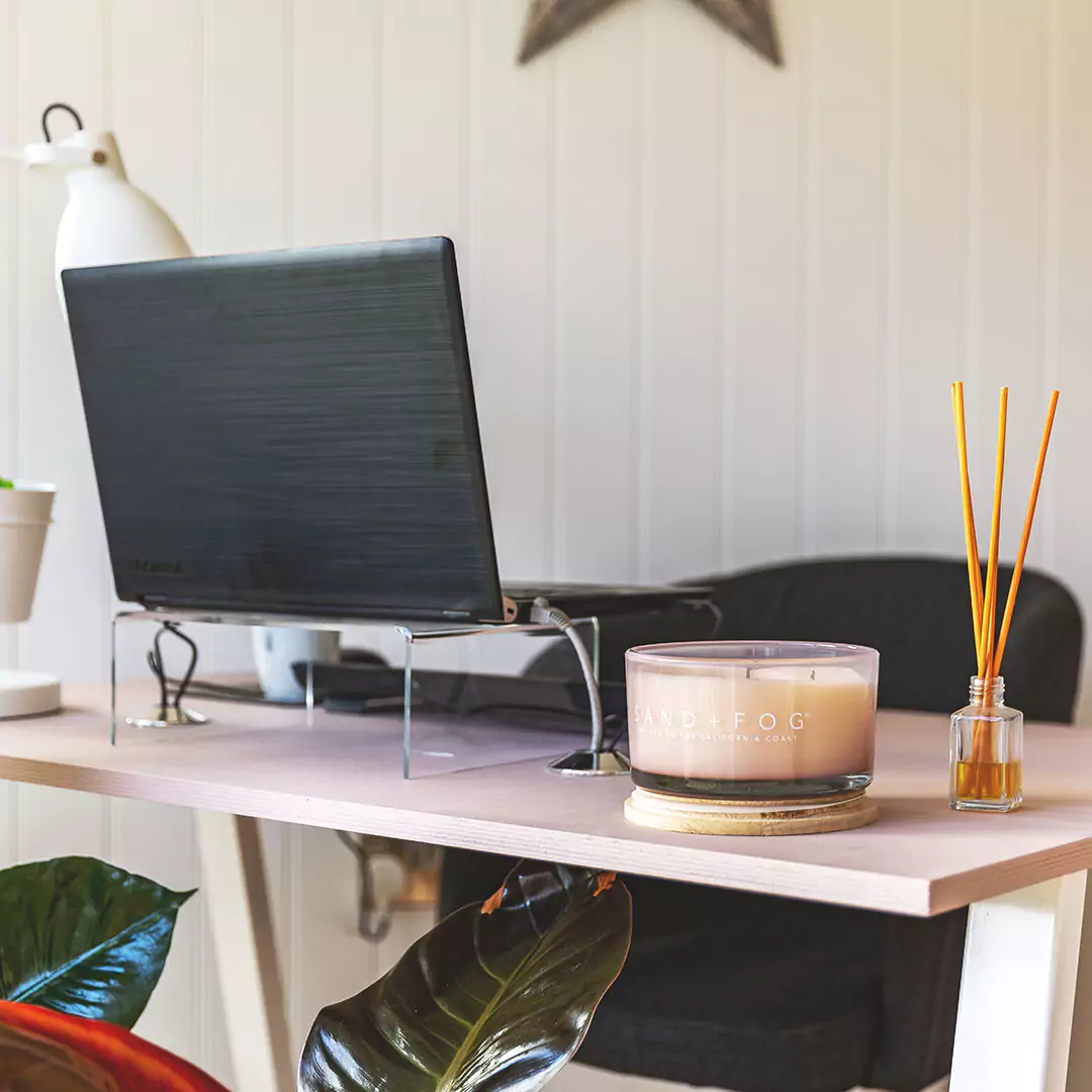 Interior of a garden office cabin with desk, laptop, lamp, candle and reed diffuser