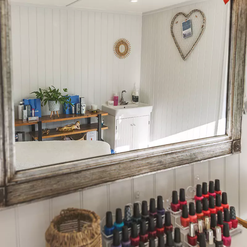 A large mirror inside a home business garden room with a collection of nail polish