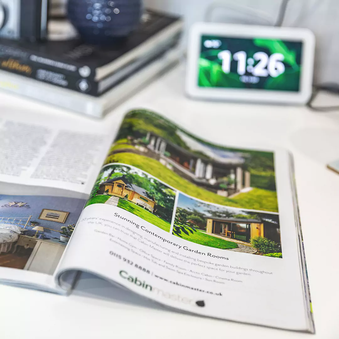 cabin master advert in magazine on desk inside garden office building with digital clock 