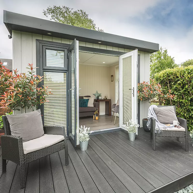 Summerhouse with doors open onto composite decking with armchairs and view into garden room