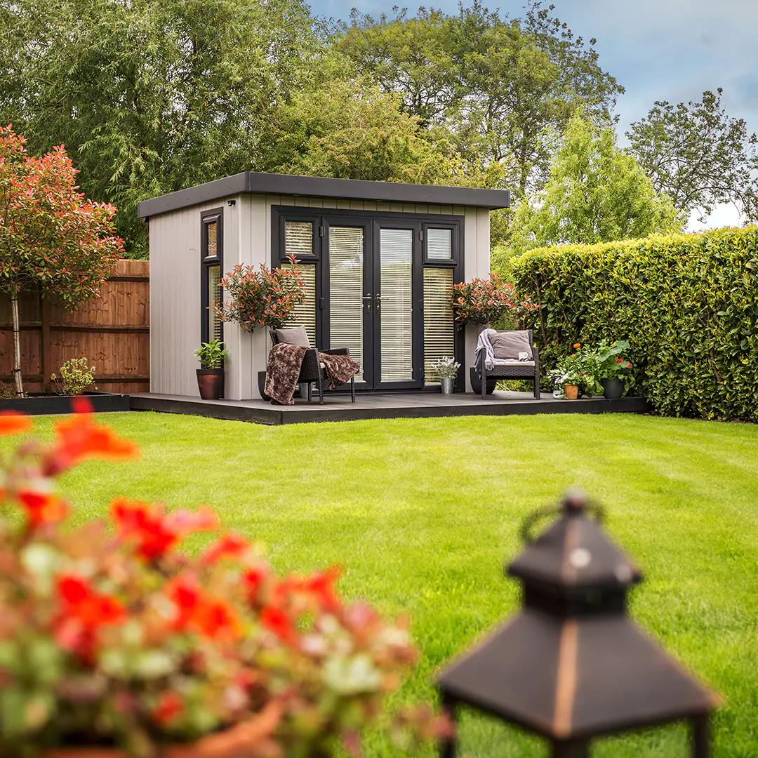 composite Summerhouse in grassy lawn area with armchairs on timber decking 