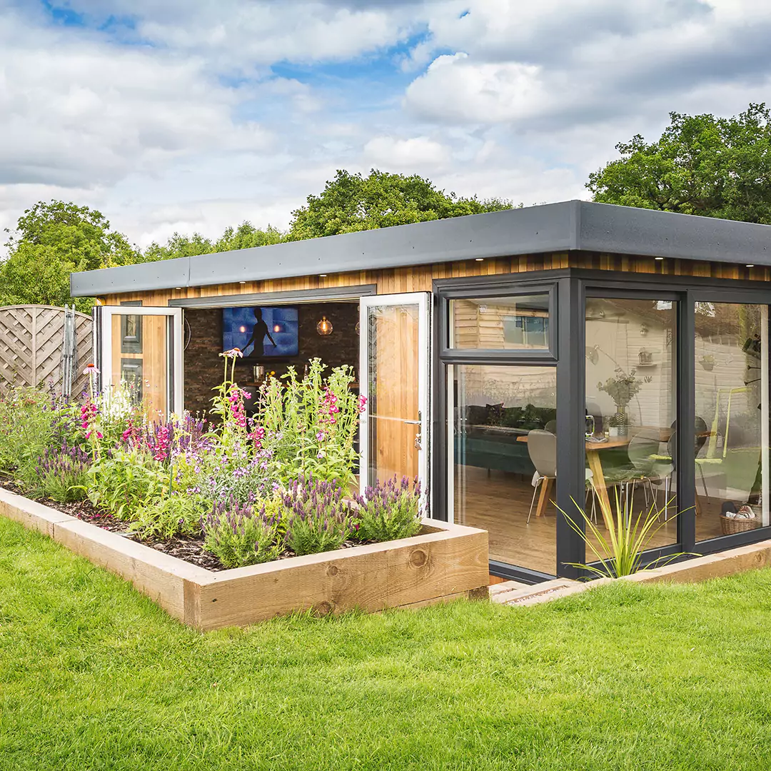 a garden area with flowers and a large timber garden bar building in the background