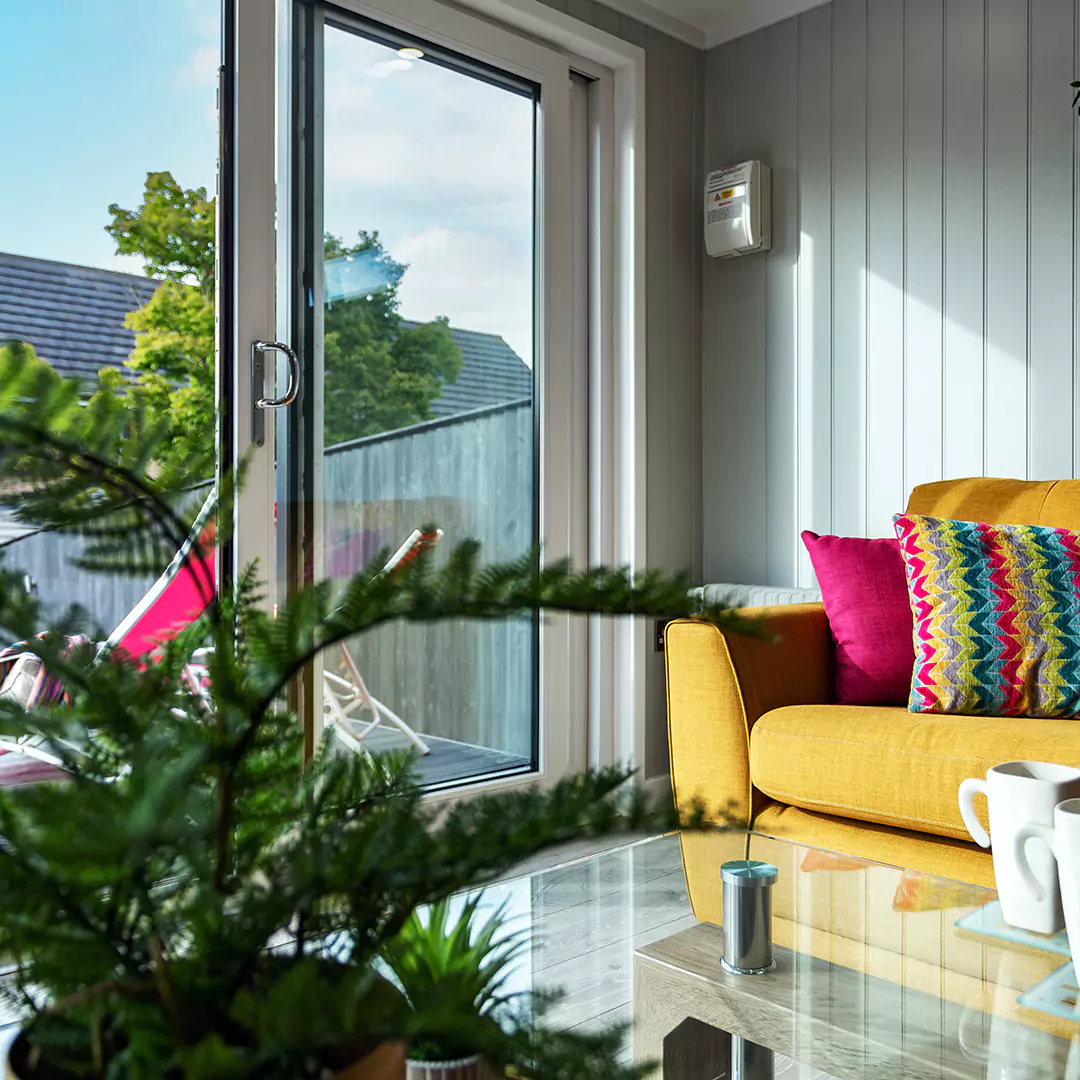 garden summerhouse with yellow couch and large green plant with brightly coloured cushions 