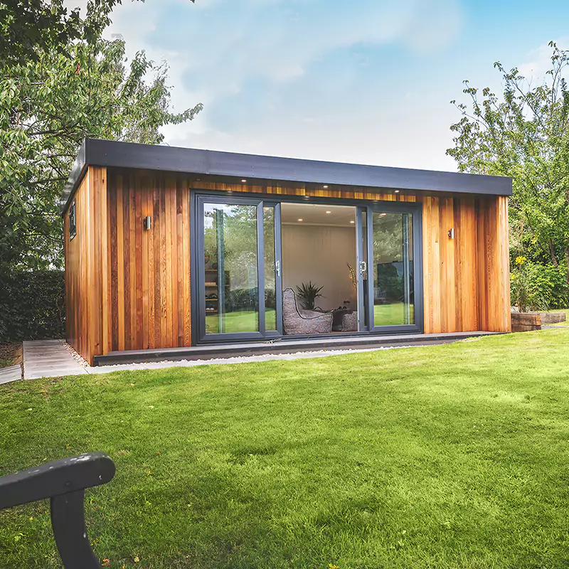 cedar garden room with doors open and large grass lawn area with view of grey sofas and furnishings